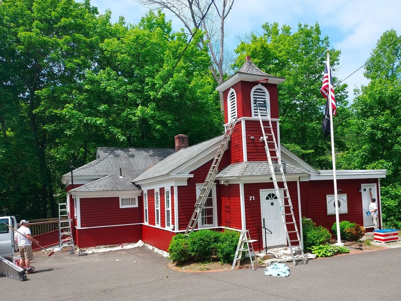 Red building being painted by two painters with ladders and rollers.