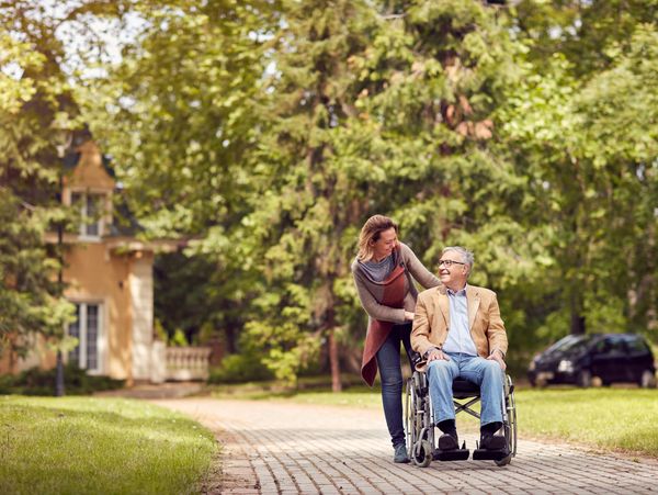 caring daughter and senior man in wheelchair on green nature walk
