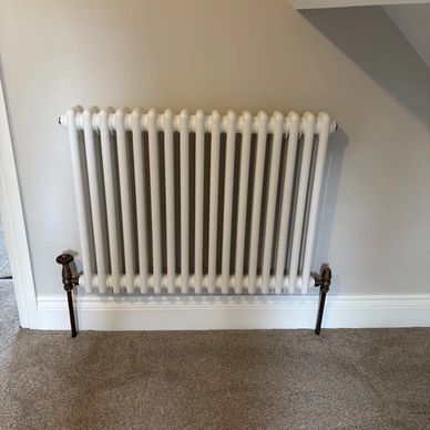 White radiator on beige wall with brown carpet.