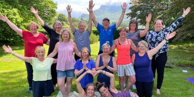 Group of people practicing yoga outdoors with arms raised.