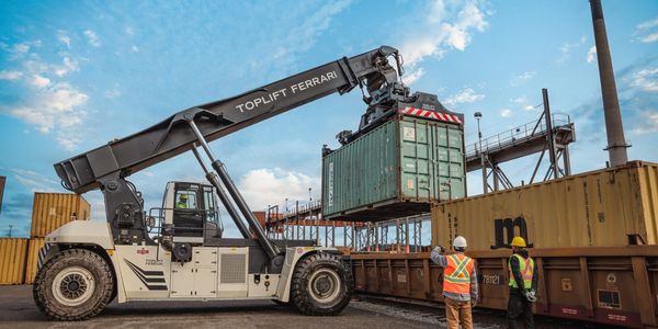 Heavy machinery loading containers with workers supervising at a shipping yard.