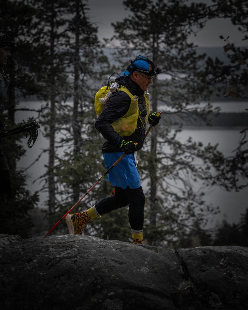 Trail runner with trekking poles and bright gear hiking over rocky terrain.