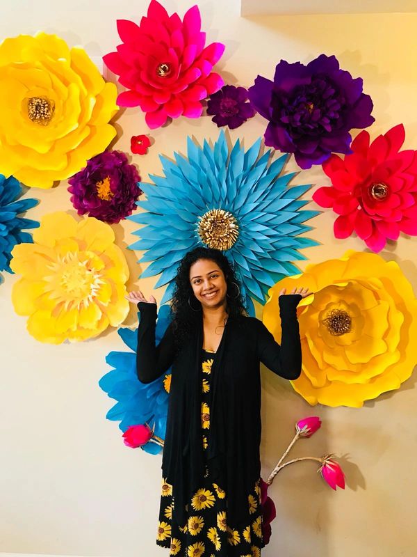 Smiling woman posing in front of a colorful large paper flower wall.