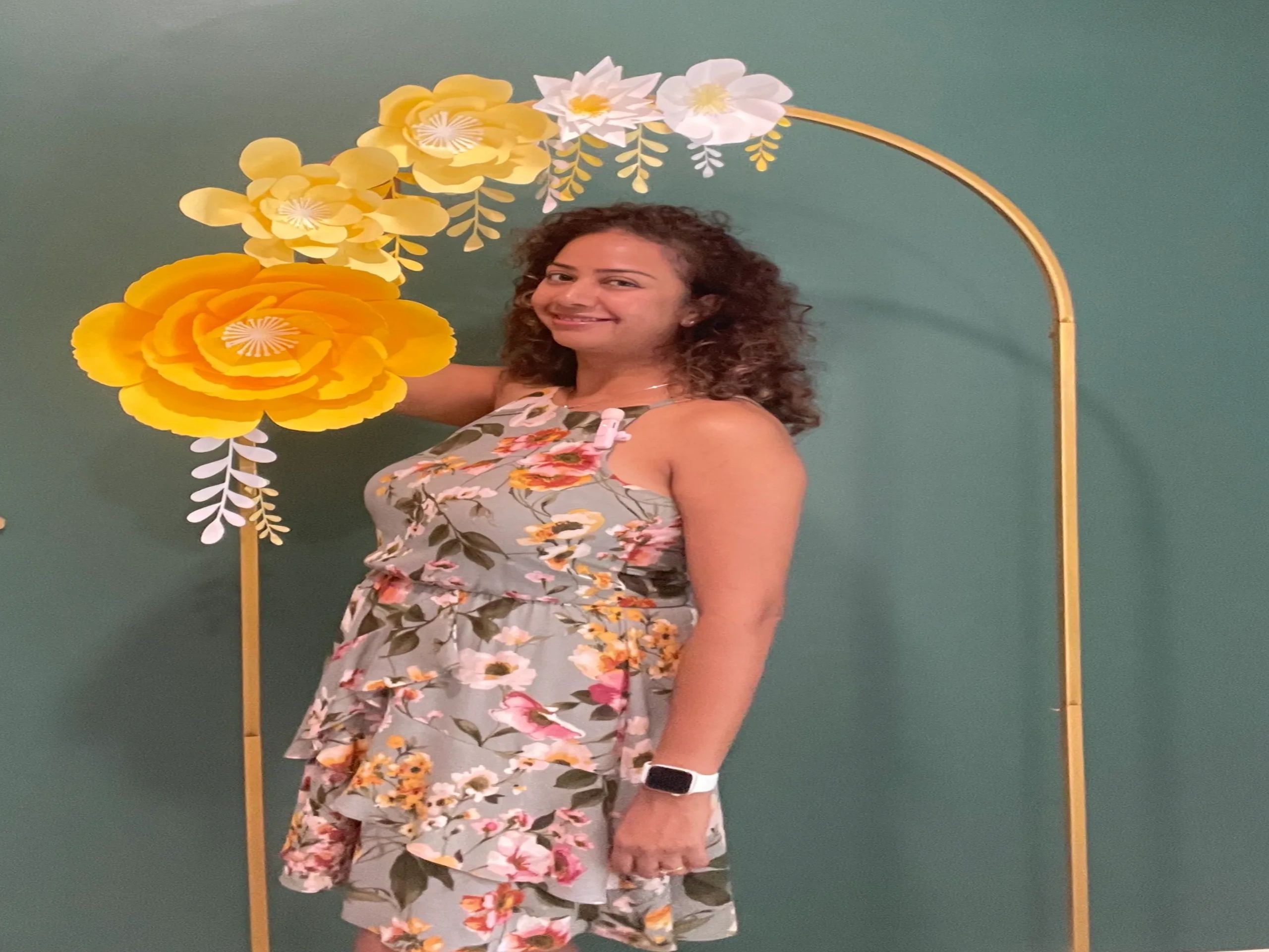 Woman in floral dress posing with a decorative yellow flower arch.