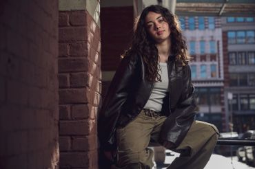Young woman in casual outfit posing against a brick wall in an urban setting.