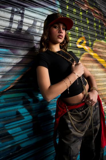 Young woman in urban streetwear poses confidently against graffiti wall.