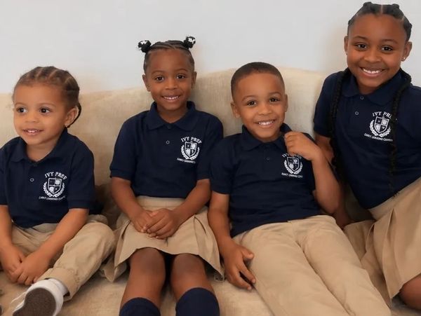 Four children in school uniforms sitting on a couch.