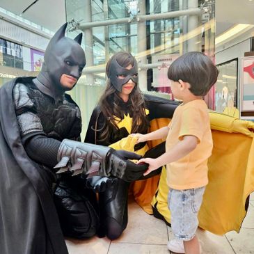 Two people in superhero costumes greet a young boy in a shopping mall.