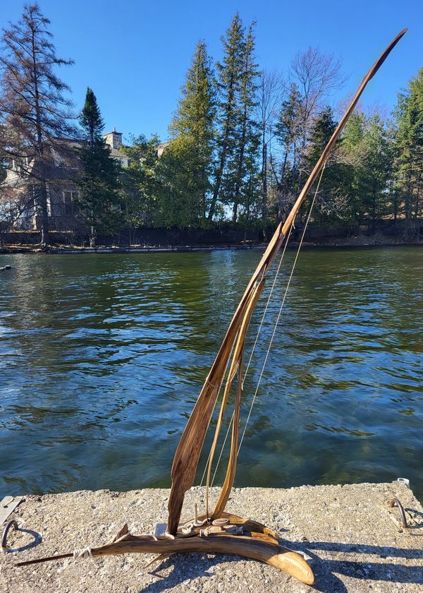 Voilier en bois sculpté, détails fins du mât et de la coque sous un ciel bleu.