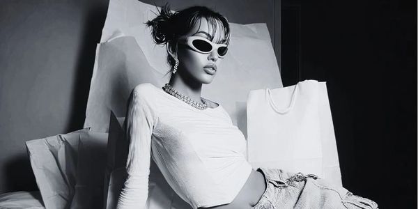 Fashionable woman in sunglasses and jeans posing with shopping bags in black and white.