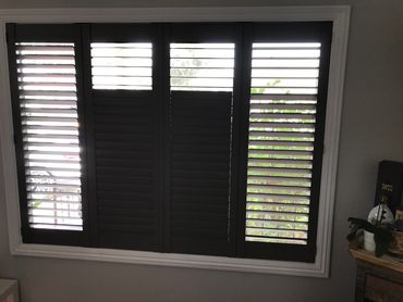 Window with black plantation shutters partially open, letting in light.