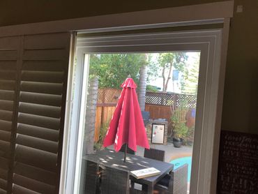 Red patio umbrella seen through a glass door by a pool.
