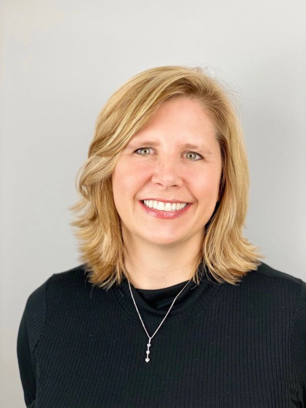 Smiling blonde woman in black top with necklace.