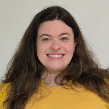Smiling woman with long brown hair in a yellow shirt.