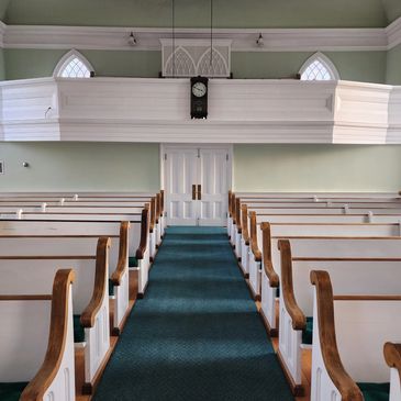 Sanctuary of the 1838 church with wooden pews, green carpet and the balcony clock