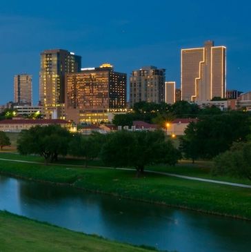 City skyline at dusk with illuminated buildings and a river.