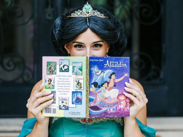 Woman dressed as Jasmine holding an Aladdin book.