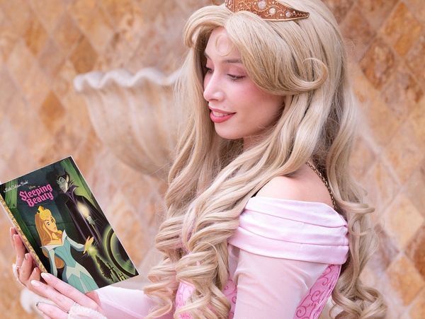 Woman dressed as Sleeping Beauty reading the storybook.