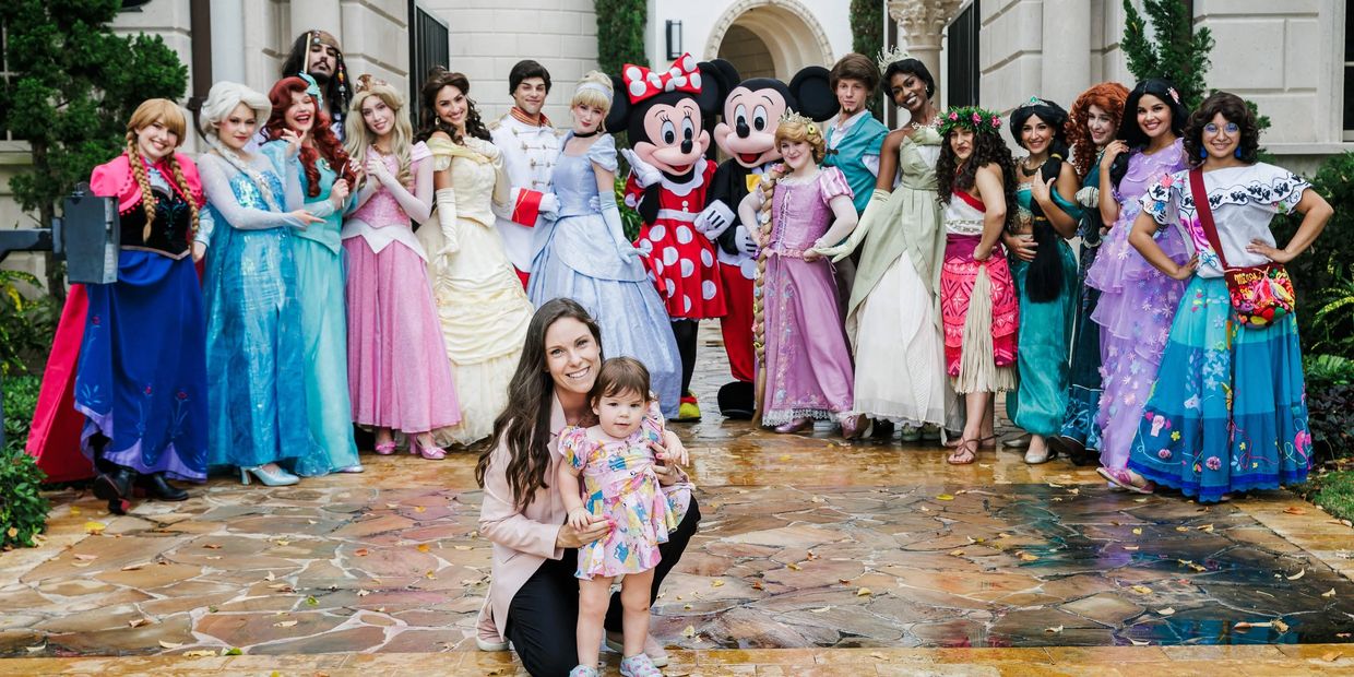 Group of people dressed as Disney characters with a woman and toddler in front.