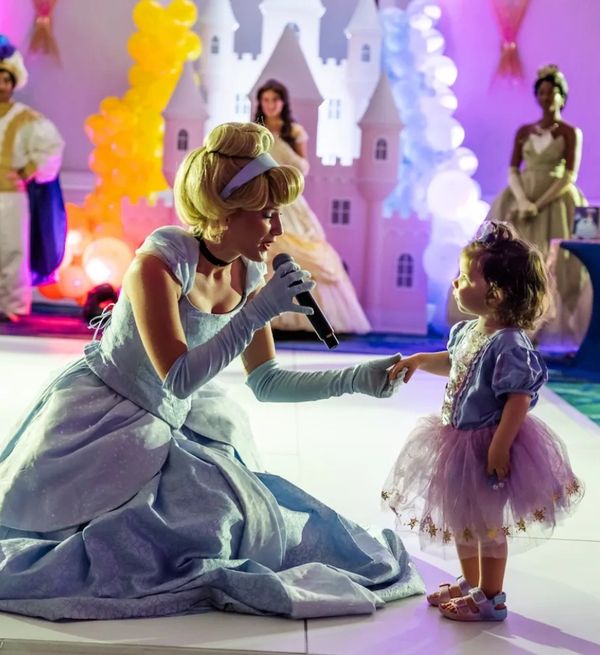 A princess character sings to a little girl at a colorful party.
