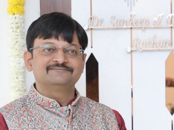 Portrait of a man wearing glasses and traditional attire, smiling gently.