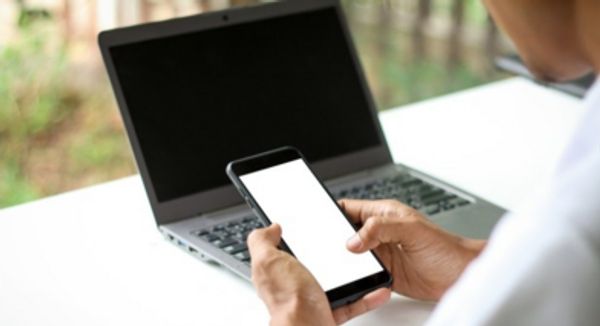 Person using a smartphone next to a laptop.