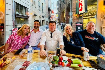 Five friends enjoying a meal together at an outdoor table in a cozy alley.