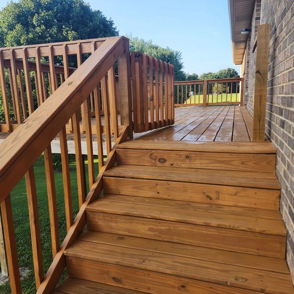 Freshly stained wooden deck and stairs with a safety gate under clear blue sky.