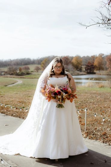 Bride in white dress holding colorful bouquet outdoors.