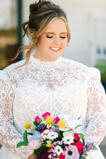 Bride in lace dress holding colorful bouquet.