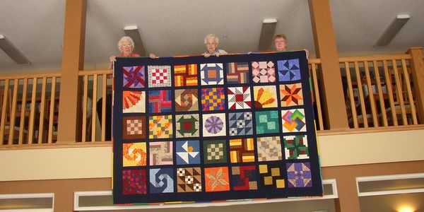 Three residents holding a huge quilt over the balcony.