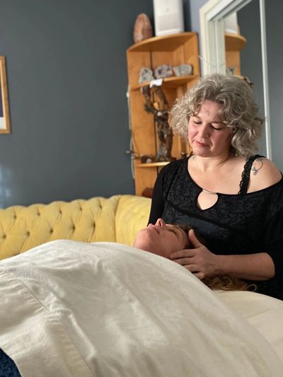 A woman giving a relaxing head massage to another woman lying on a bed.