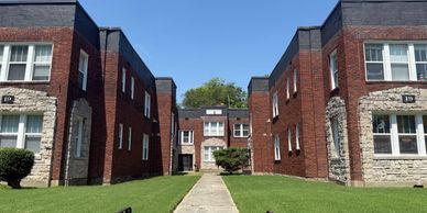 Symmetrical view of a brick apartment complex with green lawns and clear blue sky.