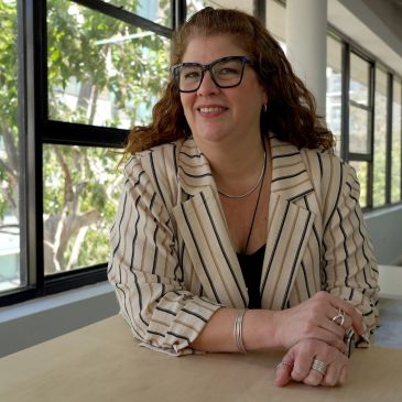 Smiling woman with glasses in a striped blazer sitting at a table.