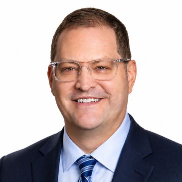 Man wearing glasses and a suit smiling at the camera.