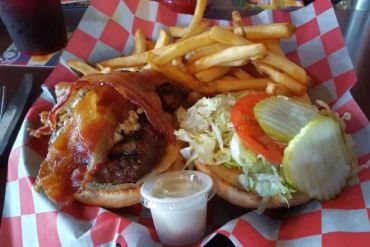 A plate of burger topped with bacon, veggies and fries 