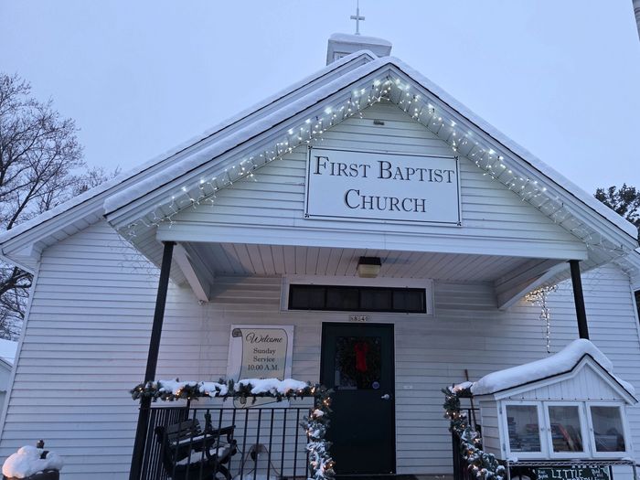 Snow-covered First Baptist Church decorated with holiday lights and a little library.