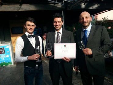 Three men dressed formally, one holding a certificate and wine glasses.