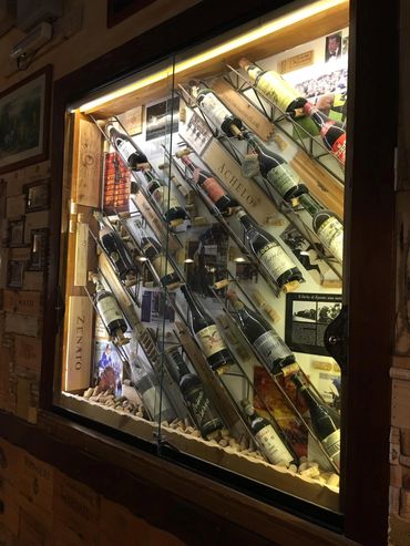 A glass display case showcasing angled wine bottles with labels and memorabilia.