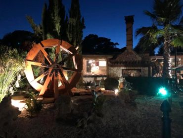 Illuminated waterwheel and rustic brick building at night in a garden.