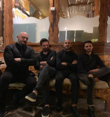 Four men in black outfits sitting on a bench inside a rustic restaurant.