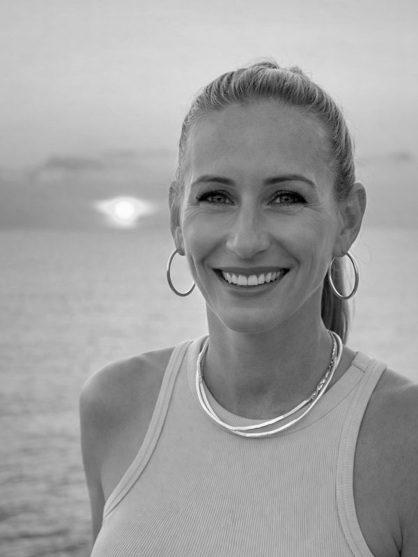Smiling woman with hoop earrings at sunset by the water.