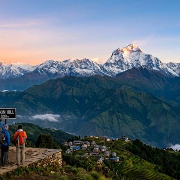 Two hikers overlooking a mountain village at sunrise from a hill.