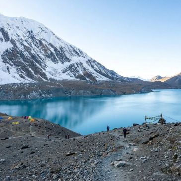 Snowy mountain overlooking a calm blue lake.