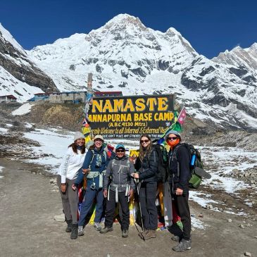 Group of hikers at Annapurna Base Camp with snowy mountains.