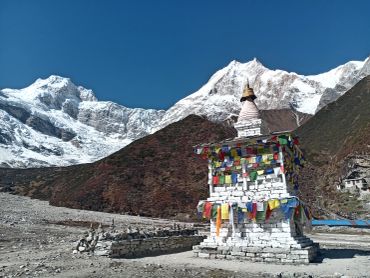 Tibetan prayer flags on a stupa with snow-covered mountains.