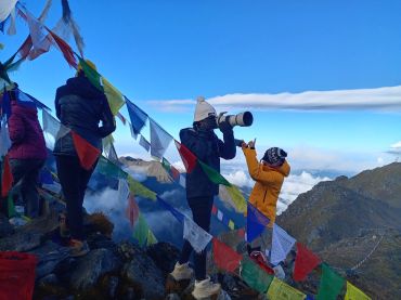 Two people with cameras among prayer flags on a mountain.