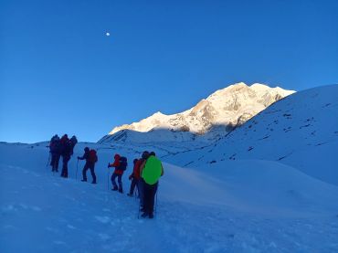 Group of hikers trekking up a snowy mountain with a clear blue sky.