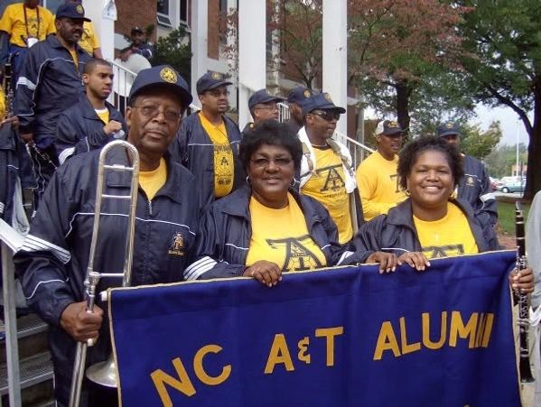 Group of NC A&amp;T alumni in band uniforms holding a banner.