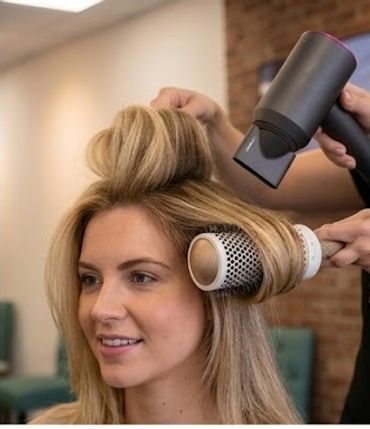 Woman getting her hair styled with a blow dryer and round brush.